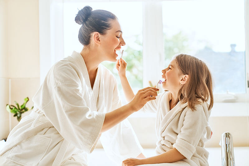 Mother and her young daughter brushing each other's teeth